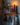 This image shows a shelf with hooks upon which sits a Greentree Petite Pillar candle in Red, lit. It sits amongst other winter items.