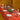 Dining table set with red tablecloth, plates, glasses, and candles in a warm-toned room.