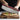 Image shows a person using the soft-grip rocking pizza cutter to cut through a pizza. The pizza is on a wooden cutting board.