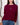 Woman wearing a burgundy sweater with button details against a white wall.