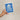 Hand holding a blue plantable seed paper envelope with white floral design on a beige background