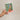 Hand holding a plantable seed paper envelope with floral design on a beige background