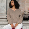 Woman sitting on a red stool wearing white pants and a beige cashmere V-neck sweater