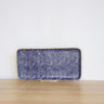 A rectangular clutch purse with a dark blue and white textured pattern, displayed on a small clear stand on a light wooden surface against a white wall.