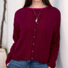 Woman wearing a burgundy sweater with button details against a white wall.