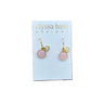 A pair of gold-tone dangle earrings with pink circular stones and small white stones, displayed on a white card labeled 'elyssa bass DESIGNS' against a red brick background.